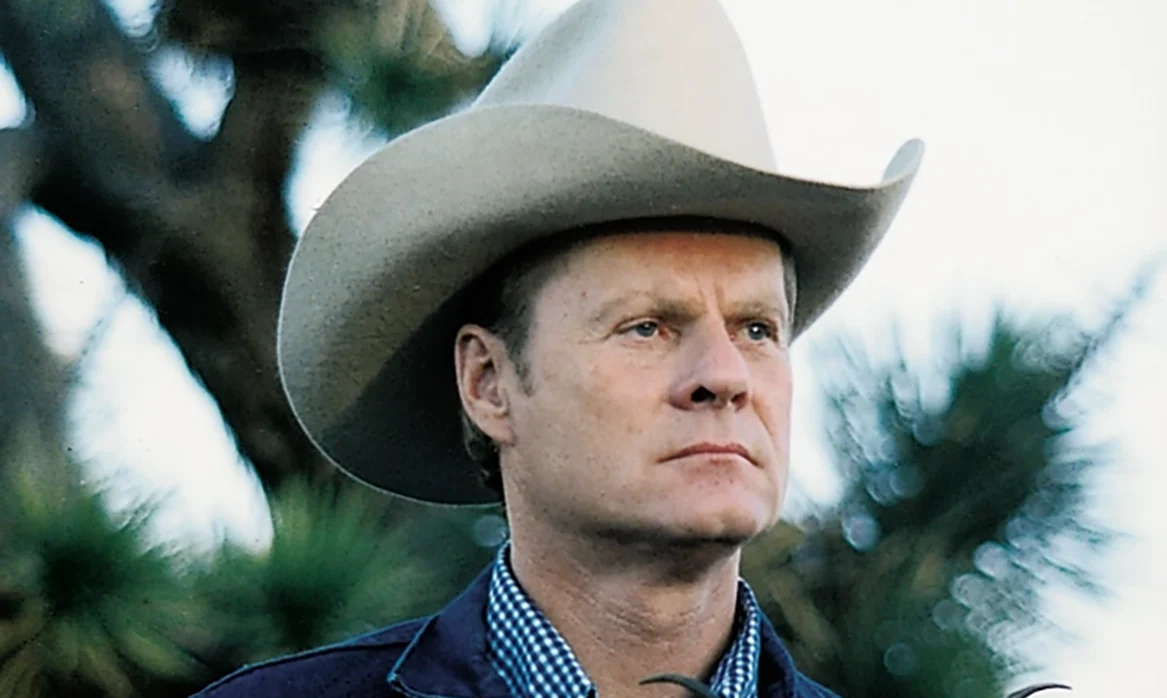 A rancher in a white cowboy hat holds a small bronze sculpture of a longhorn steer.