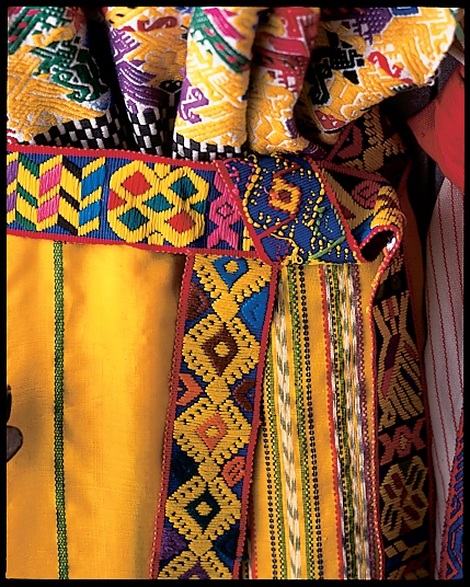 Close-up of a bright yellow textile with a multicolored geometric woven sash.
