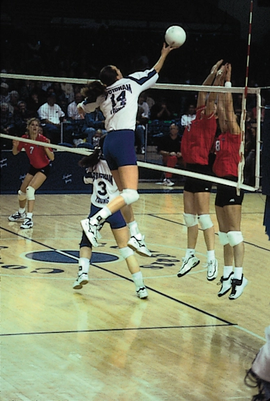 Volleyball player in a white uniform jumps at the net to spike the ball during a match.