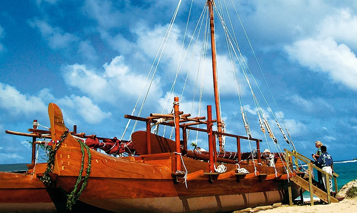 A large, wooden double-hulled canoe sitting on a beach.