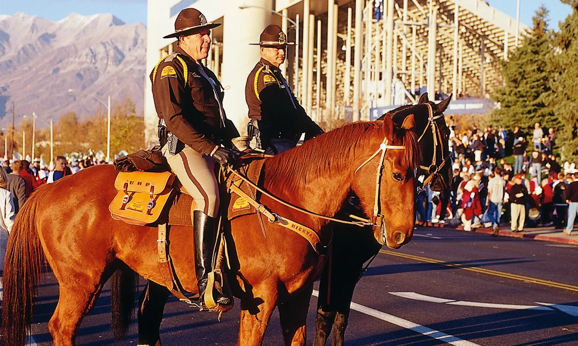 Two men in high way patrol uniforms sit on horses in front of the BYU stadium.