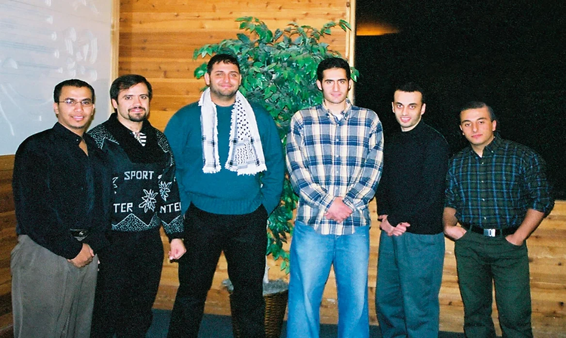 Six men stand together in a cabin-like structure.