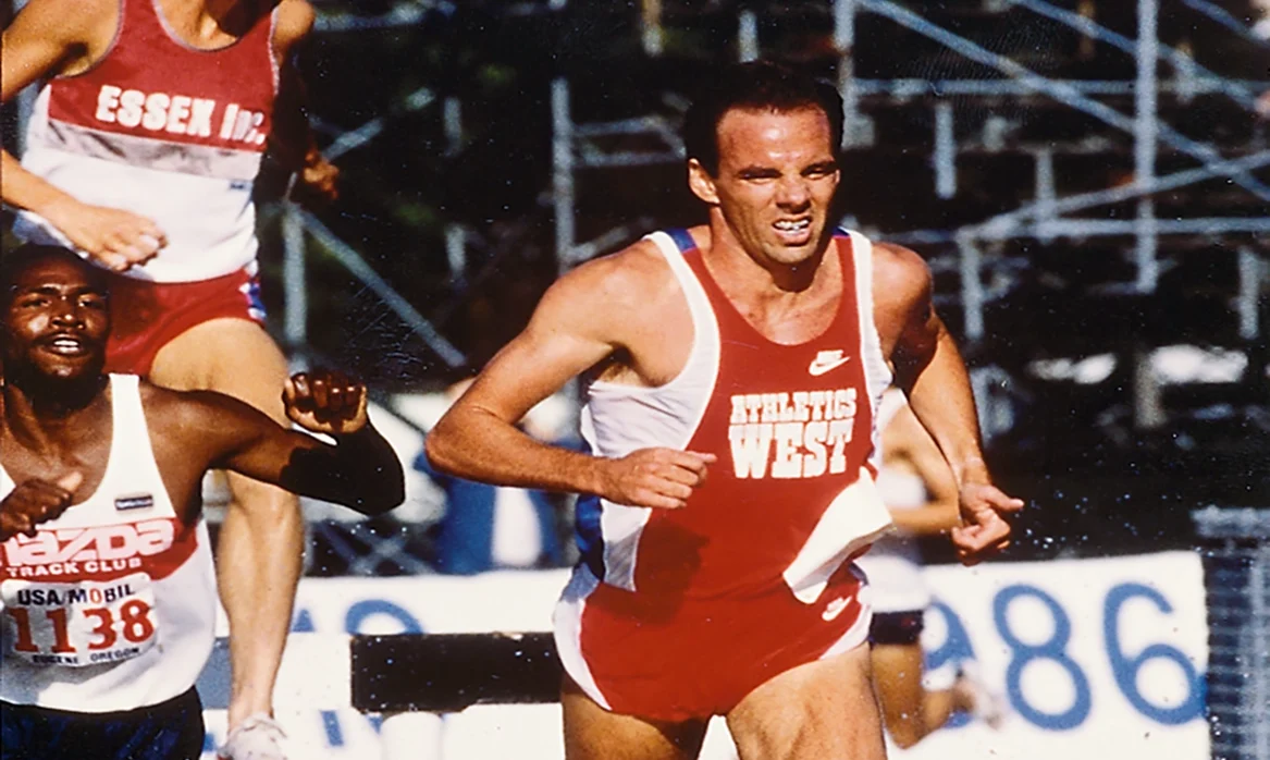 Henry Marsh running down a track with hurdles on it