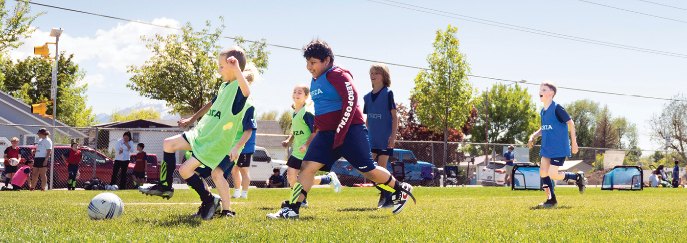 Children run after a soccer ball on a grass field.