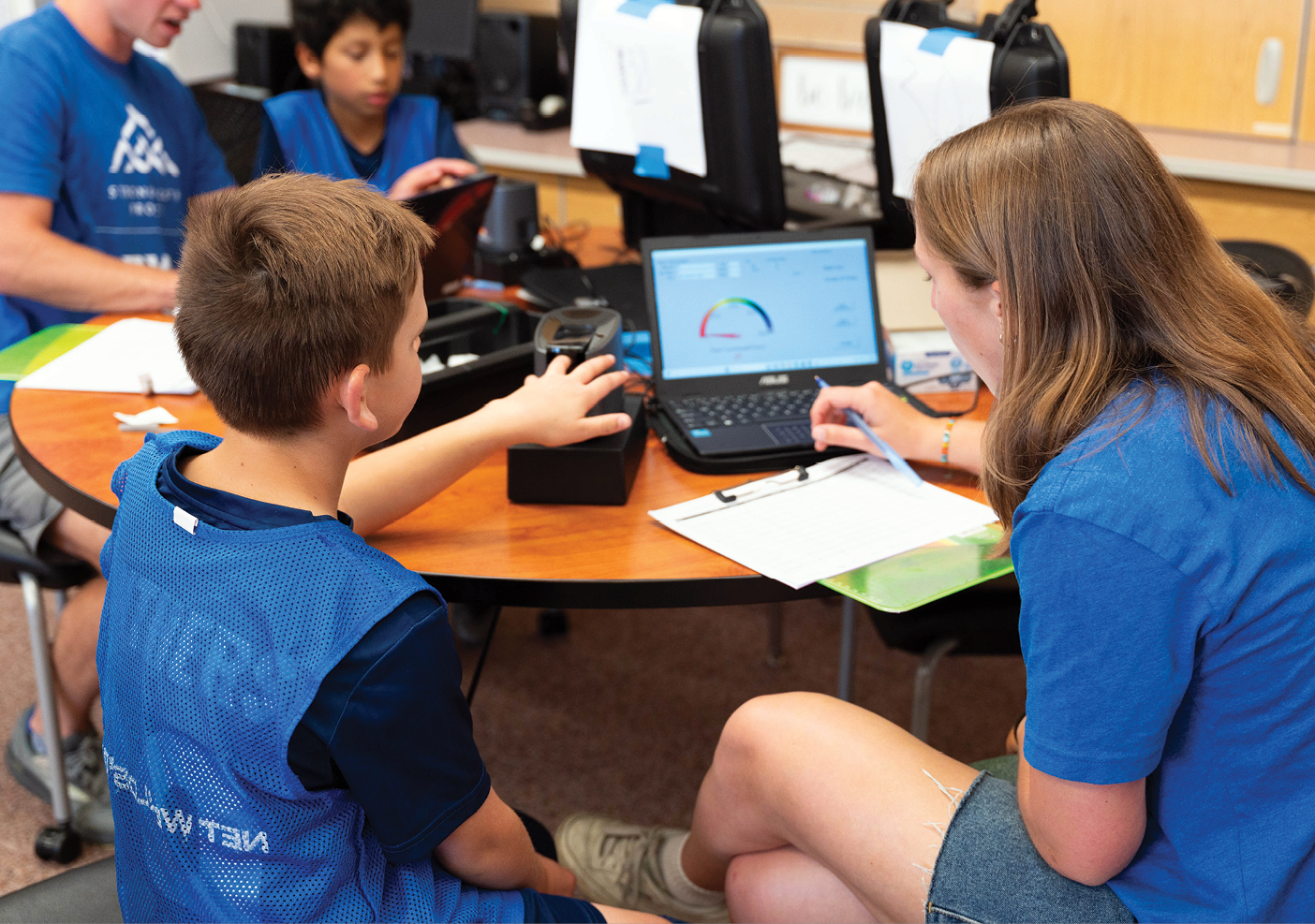 A BYU student sits at a table with a young boy and teaches him principles of physical fitness.
