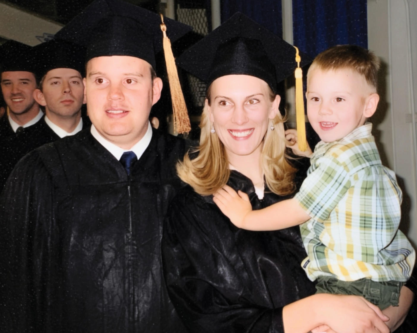 A young boy is held by his mother, who is wearing graduation robes. His father, also robed, is also in the photo.