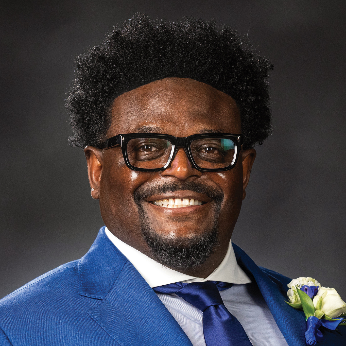 Derwin Gray smiles for a portrait, wearing a blue suit coat.