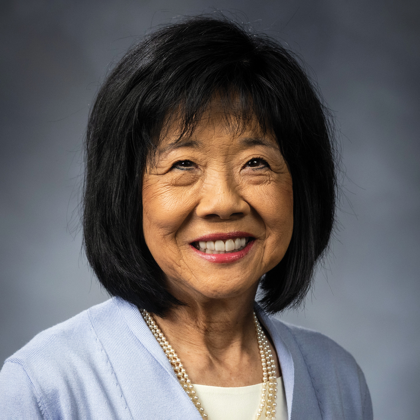 Ann Takasaki poses for a portrait against a gray background.